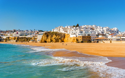 Sandstrand vor der weißen Stadt Albufeira an der Algarve in Portugal mit Felsen im Hintergrund.
