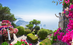 Blumenreicher Garten mit Blick auf das Meer und eine Statue auf einem sonnigen Tag.