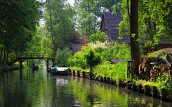 Ländlicher Wasserweg mit Brücke und üppiger Vegetation bei Sonnenschein.