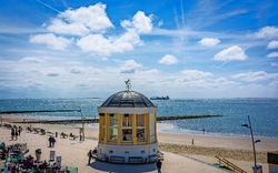 Pavillon am Strand mit Meer im Hintergrund und wenigen Menschen.