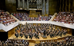 Ein Orchester spielt vor einem großen Publikum in einem Konzertsaal.