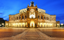 Historisches Opernhaus bei Abenddämmerung, beleuchtet vor blauem Himmel.