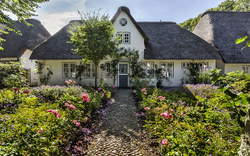 Reetgedecktes Haus im Garten mit blühenden Blumen und Kopfsteinpflasterweg.