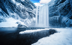 Ein gefrorener Wasserfall in einer eisigen Landschaft unter blauem Himmel.